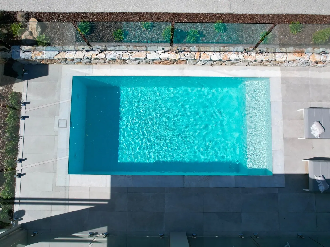 Overhead view of a rectangular plunge pool with a full width bench seat along one end, stone coping all round and a dry stone retaining wall alongside.